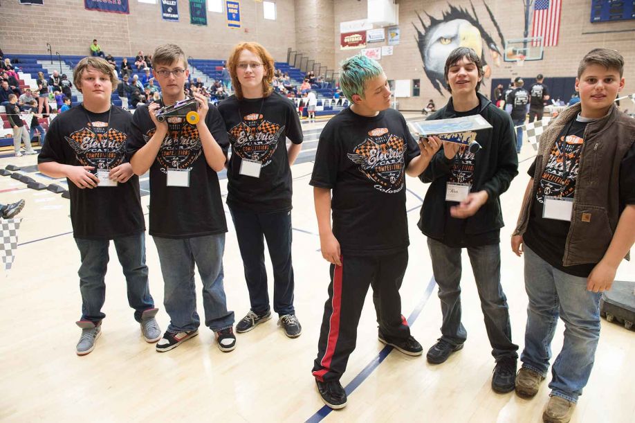 Six young boys stand, as two hold model racecars inside a gym.