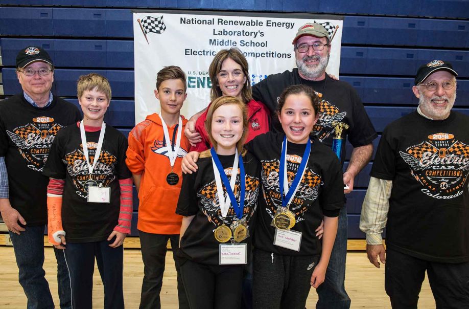 Two young girls smile wearing medals while two boys and four adults smile behind them in a gym.