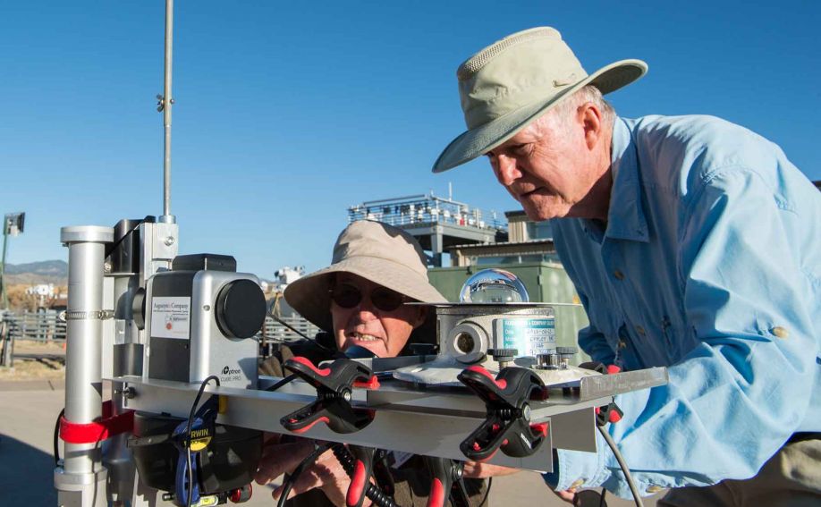 Two men hunch over solar radiation instruments outdoors.