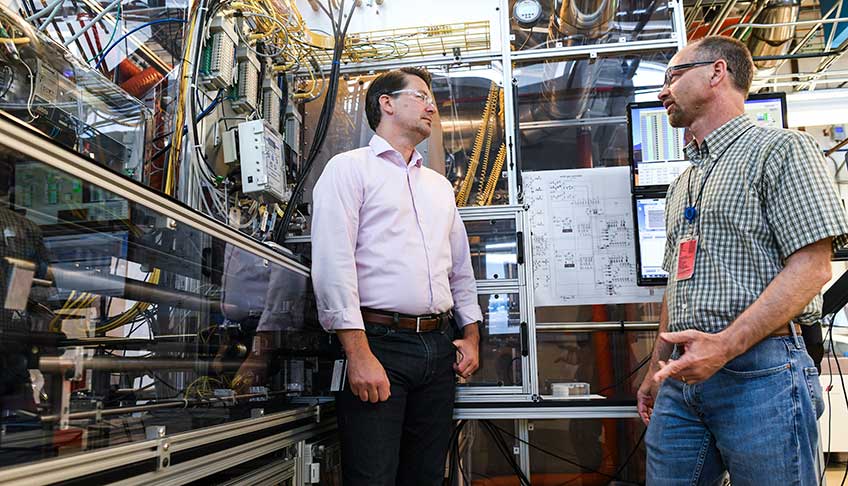 Two men stand near a piece of laboratory equipment.